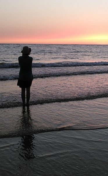 Olivia's silhouette standing in the ocean watching the sun set on her spiritual journey.