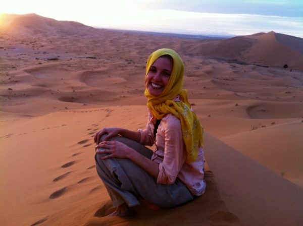 Olivia with a head wrapping sitting on a desert dune.