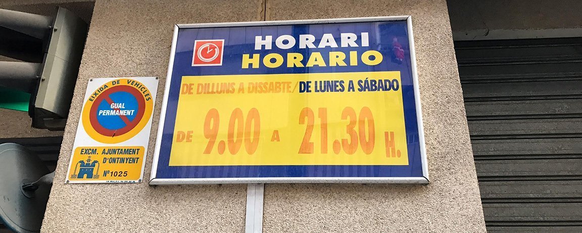 Bilingual sign in Ontinyent, Valencia showing a supermarket’s operating hours and day