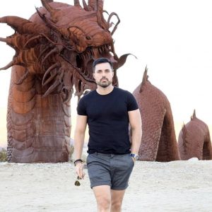 Marcos, hospitality professional, walking on the beach in front of a statue of a sea monster in Borrego Springs, California.