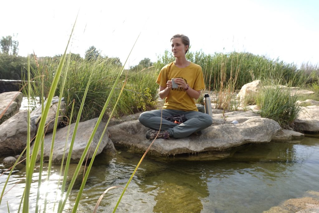 Olivia practicing mindfulness on a rock above a river.