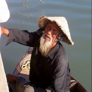 An older man in a boat wearing a rice hat.