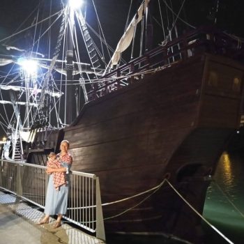 Kristen as a new mom abroad in front of an old wooden ship