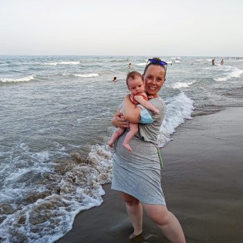 Kristen as a new mom abroad at the beach with her baby